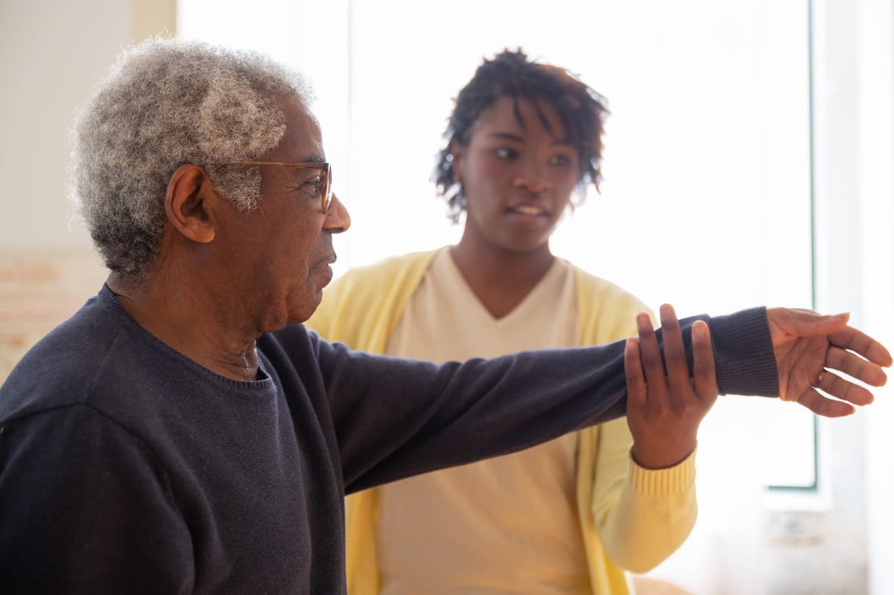 services-03 A caregiver helps an elderly man with arm exercises in a warm and caring environment.