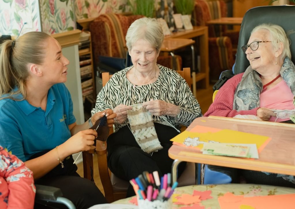 caregiver-assists-two-elderly-women-knitting-gstffdroygo caregiver-assists-two-elderly-women-knitting-gstffdroygo
