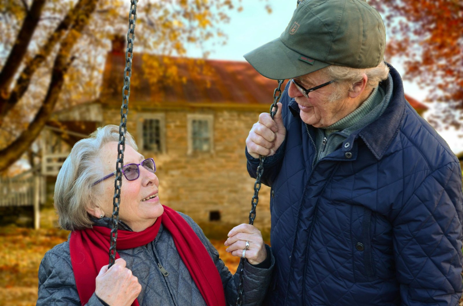 Effective Communication Between Seniors, Families, and Caregivers A happy elderly couple sharing a joyful moment on a swing in autumn setting.