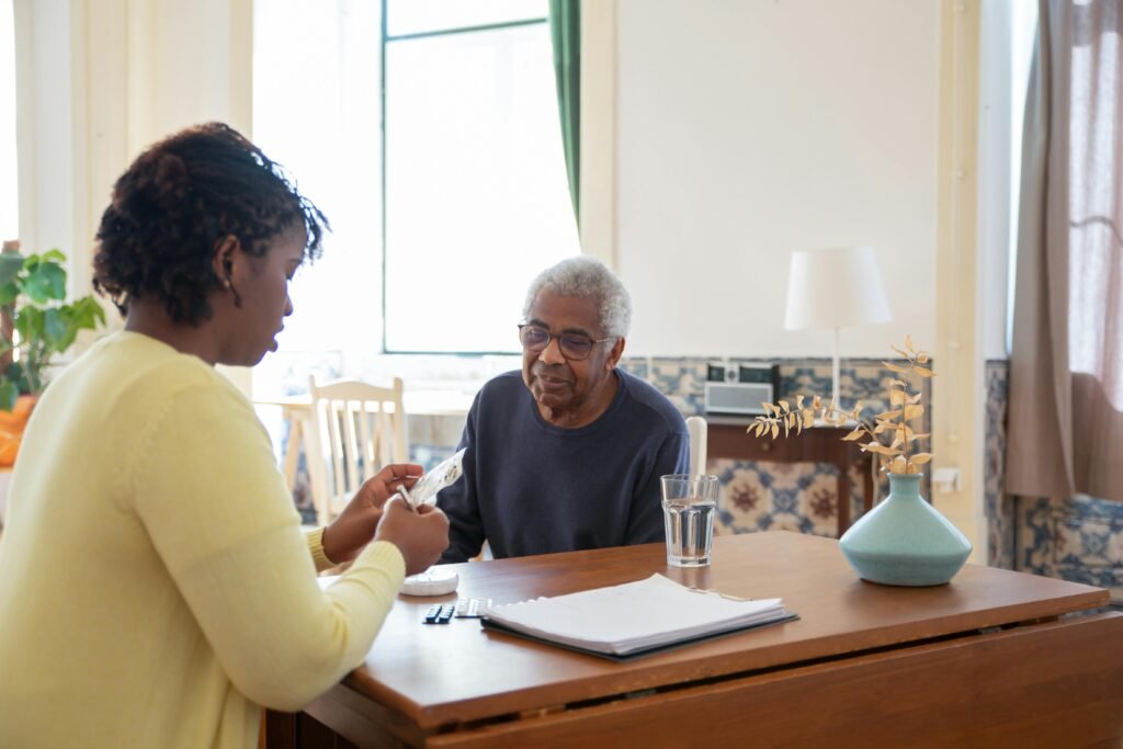 pexels photo 7551668 7551668 A caregiver assists an elderly man with medication in a warm, sunlit living room.